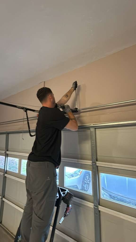 Two technicians on orange ladders working at the header above a garage door, seen from inside the garage