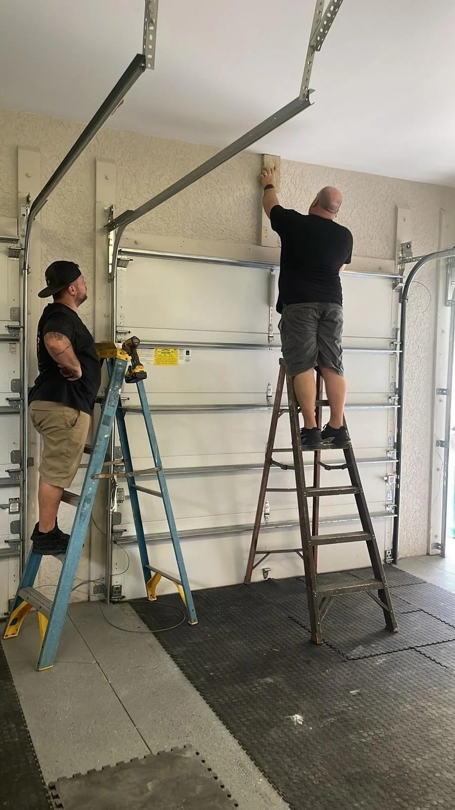 Technician on a stepladder checking the spring shaft above a garage door with decorative windows