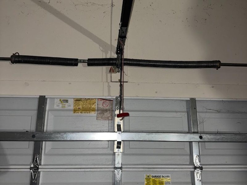Close view of a spring and center bracket above a garage door with steel rails below