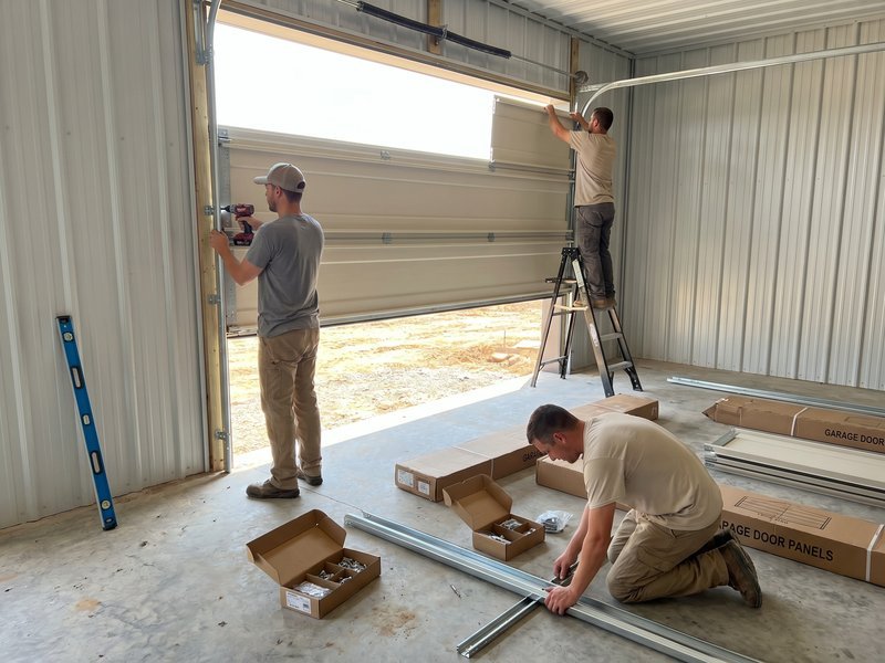 Workers assembling new track parts and door sections with open boxes on a garage floor