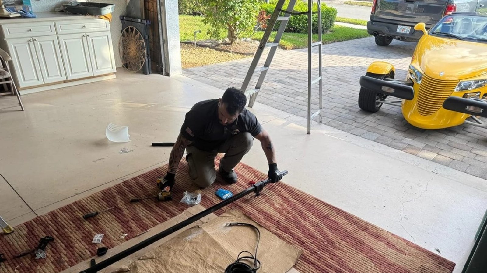 Technician kneeling on a red rug beside a long metal rod laid across the garage floor